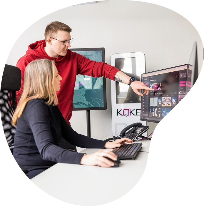 Eine Frau und ein Mann schauen auf einen Computerbildschirm und sprechen über das Content-Management-System KMS von KOKE